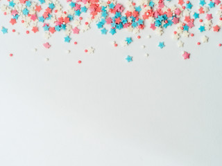 Festive border frame of colorful pastel sprinkles on white background, copy space bottom. Sugar...