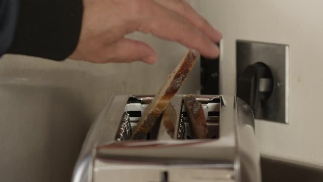 Toasted bread jumping out of silver vintage retro style bread toaster. Male hand taking bread out.