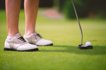 Golfers hit the ball on the green grass, putting it into the hole.
