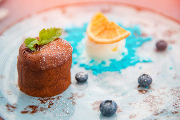 Chocolate fondant dessert pudding with blue ice cream on plate with orange