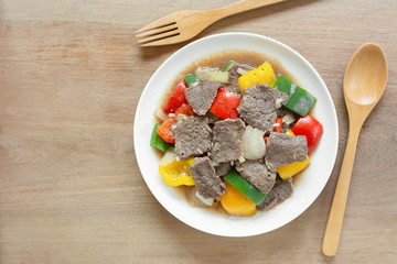 top view of stir fried beef with black and sweet pepper in a ceramic dish on wooden table. homemade style food concept.
