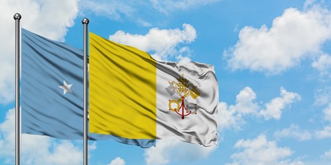 Micronesia and Vatican City flag waving in the wind against white cloudy blue sky together. Diplomacy concept, international relations.