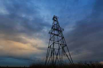 Old oil rig, profiled on sky with storm clouds, at sunset