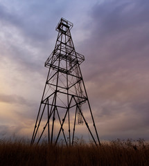 Old oil rig, profiled on sky with storm clouds, at sunset