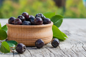 Black ripe berries of food, medicinal shrub Aronia, chokeberry (Aronia melanocarpa) in a wooden plate on an old wooden table, rustic style, close-up, healthy food concept, copy of space