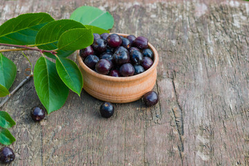 Black ripe berries of food, medicinal shrub Aronia, chokeberry (Aronia melanocarpa) in a wooden plate on an old wooden table, rustic style, close-up, healthy food concept, copy of space