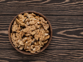 Walnuts on wooden dark plate on wooden brown background top view