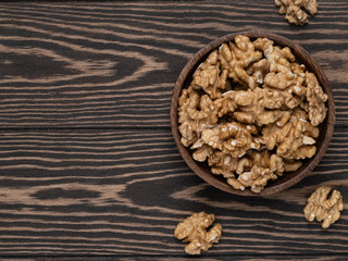 Walnuts on wooden dark plate on wooden brown background top view