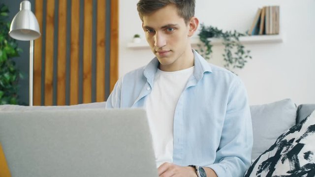 Close  up of young man seat on couch in living room and work on laptop. Freelance e-learning concept. 4k slow motion footage.