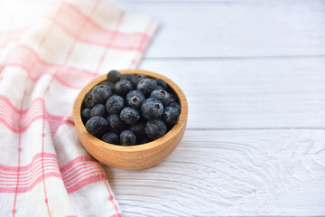 Fresh Blueberry with drops of water in wooden bowl on white wooden table. Blue berry detail. Top view. Concept of healthy and dieting eating. Blueberry antioxidant. Selected focus. Copy space.