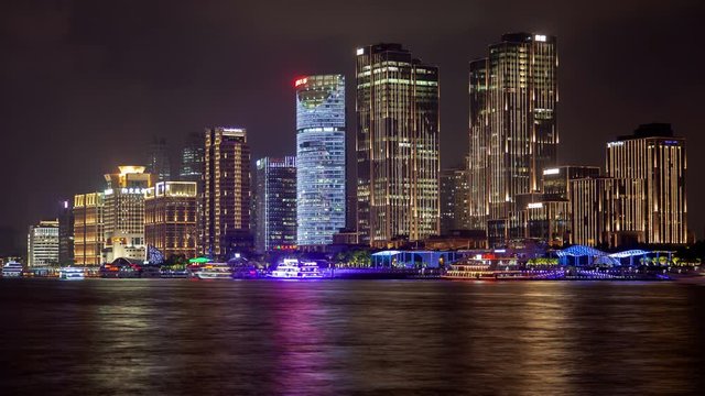 Timelapse illuminated Chinese motorboats sail along Huangpu river against modern city buildings and skyscrapers reflecting lights on water at night in Shanghai