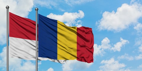 Monaco and Romania flag waving in the wind against white cloudy blue sky together. Diplomacy...