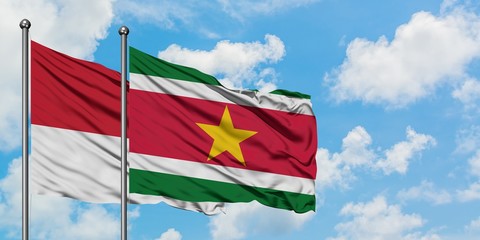 Monaco and Suriname flag waving in the wind against white cloudy blue sky together. Diplomacy concept, international relations.
