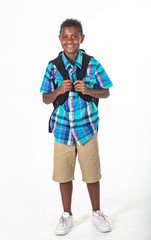 Smiling African American school boy isolated on white background. Wearing a backpack and a plaid shirt and ready to go to school. Front view © Brocreative