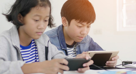 Boy and girl playing with smart phone and tablet computer at home.
