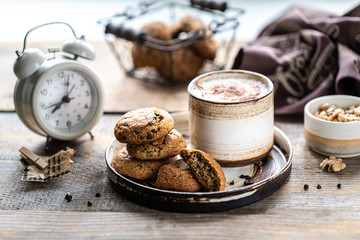 Homemade cookies with nuts and coffee in a ceramic cup on a wooden table. Time to drink some coffee. Alarm clock in the background. Breakfast