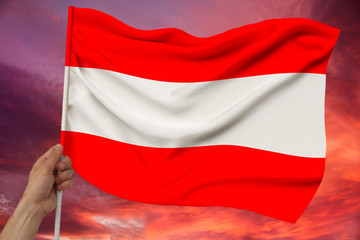 male hand holds against the background of the sky with clouds the national flag of Austria on a luxury satin texture, silk with waves, closeup, copy space
