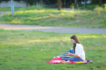 lady sitting in the park and talking on Skype via a laptop with headphones