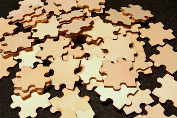 Chaos and confusion: detail of wooden jigsaw puzzle pieces mixed on black background. Concept for disorganization and problems.