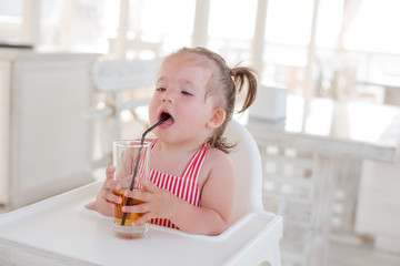A little smiling toddler girl is sitting at a table in a summer cafe in the seaside resort.
