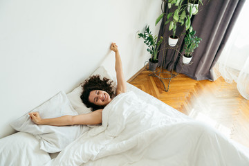 young pretty woman in bed with white sheets bright light