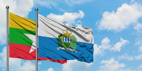Myanmar and San Marino flag waving in the wind against white cloudy blue sky together. Diplomacy...