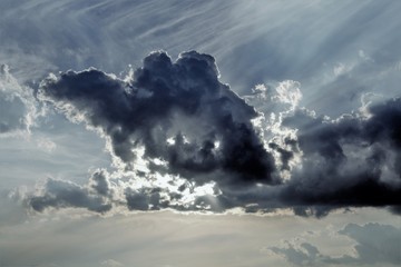 evocative image of the sun hiding behind a large dark cloud at sunset