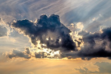 evocative image of the sun hiding behind a large dark cloud at sunset