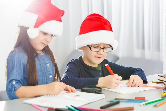 Writing letter to santa. Children in santa hats make wish list of presents for christmas. Winter holidays. Boy and girl, brother and sister draw