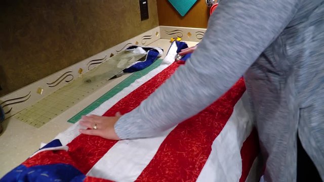 Woman prepares handmade quilt for binding by trimming off excess material using a rotary cutter; pattern is Stars and Strips; for the Quilt of Valor program to show appreciation for military veterans