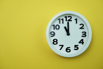 White round clock showing eleven o'clock on yellow background