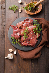 Raw chicken liver on slate board on  wooden background. Garnished with herb parsley and pepper. Food ingredient