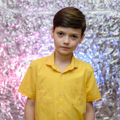 Holiday photo concept for teenager boy. Portrait of a baby boy on a shiny background in a yellow shirt. Stands in front of the camera in different poses with emotions.