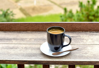 Fresh brewed coffee cup with saucer placed on wooden bar in a resort with natural countryside background.