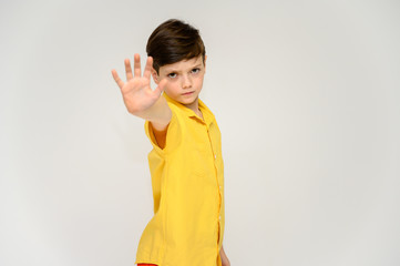 Obraz premium Concept boy teenager shows imitates the behavior of heroes from different movies. Portrait of a child on a white background in a yellow shirt. Standing in front of the camera in poses with emotions.