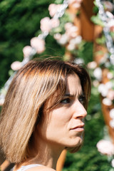 Vertical photo of a blonde girl with worried expression sitting on a rocking chair decorated with roses in a garden