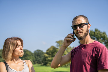 Girl looking at a boy with a serious expression who talks to the mobile looking at the front in a garden