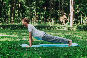 Young attractive man goes in for sports or yoga on the lawn in the park, does the straight arm strap exercise.