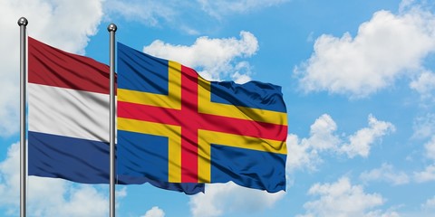 Netherlands and Aland Islands flag waving in the wind against white cloudy blue sky together. Diplomacy concept, international relations.