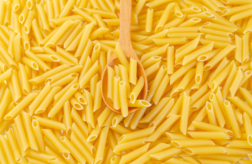 Penne rigate pasta pile background with wooden spoon.