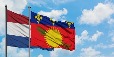 Netherlands and Guadeloupe flag waving in the wind against white cloudy blue sky together. Diplomacy concept, international relations.