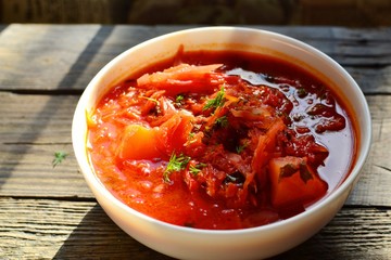 Ukrainian and Russian cuisine, red borsch. Tomato soup. Vegetable borscht made from tomato, bell pepper, parsley, onions, potatoes, carrots, cabbage and beets. Food on a wooden background.