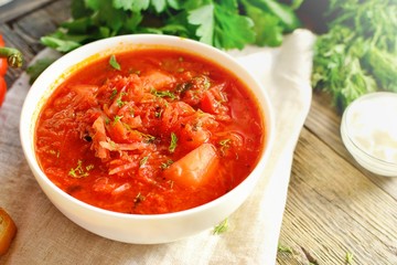 Ukrainian and Russian cuisine, red borsch. Tomato soup. Vegetable borscht made from tomato, bell pepper, parsley, onions, potatoes, carrots, cabbage and beets. Food on a wooden background.