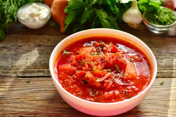 Ukrainian and Russian cuisine, red borsch. Tomato soup. Vegetable borscht made from tomato, bell pepper, parsley, onions, potatoes, carrots, cabbage and beets. Food on a wooden background.