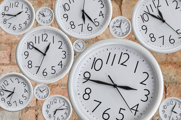 Set of white analog round office clocks of different sizes showing various time against the background of a red brick wall