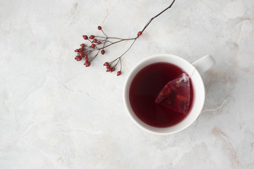 Fruity tea in tea pyramid bag in white cup and red berries on marble background. Cozy winter mood, top view