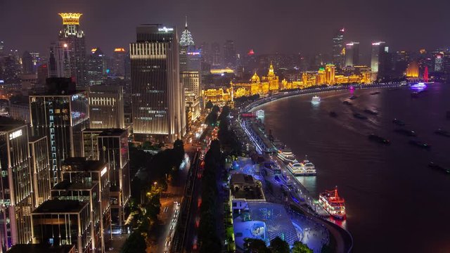 Timelapse famous Waitan with Shanghai motorboats at piers and sailing along wide calm Huangpu river reflecting city lights at night in China
