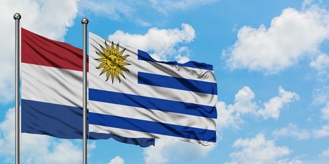 Netherlands and Uruguay flag waving in the wind against white cloudy blue sky together. Diplomacy concept, international relations.