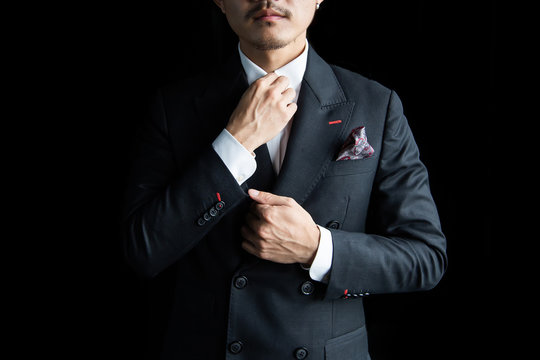 Asian businessman in a black suit is standing on a black background and has space for add text. Black suit for business people and use for formal work.