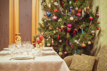 Beautiful decorated Christmas tree and festive table in living room interior with sofa and door. Concept of new year holiday at cozy home. Vintage tone